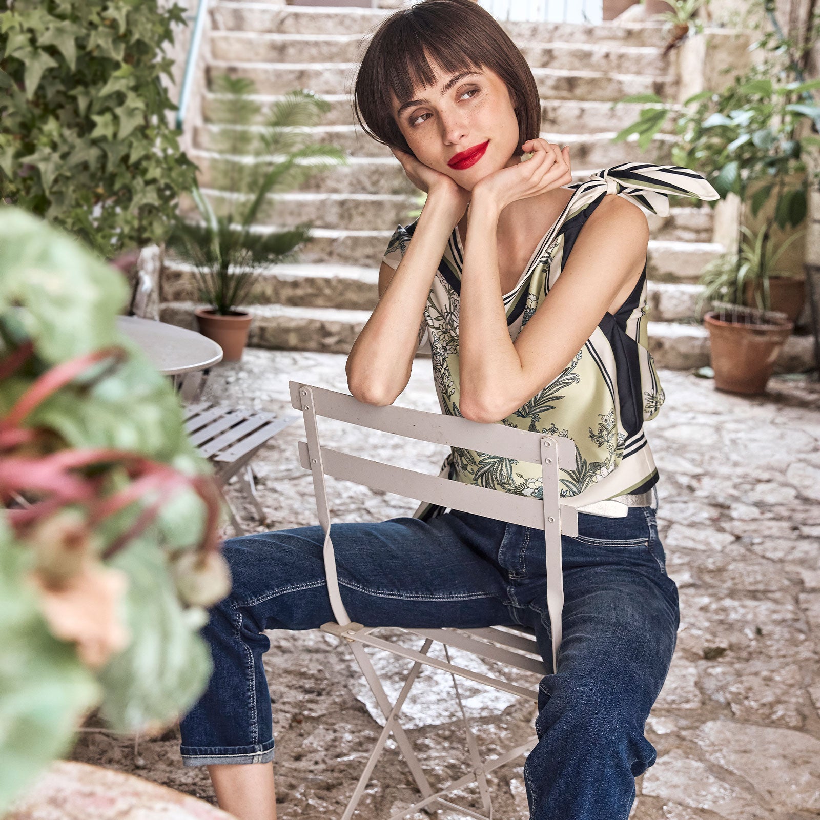 Woman in printed top and denim jeans at a charming courtyard café
