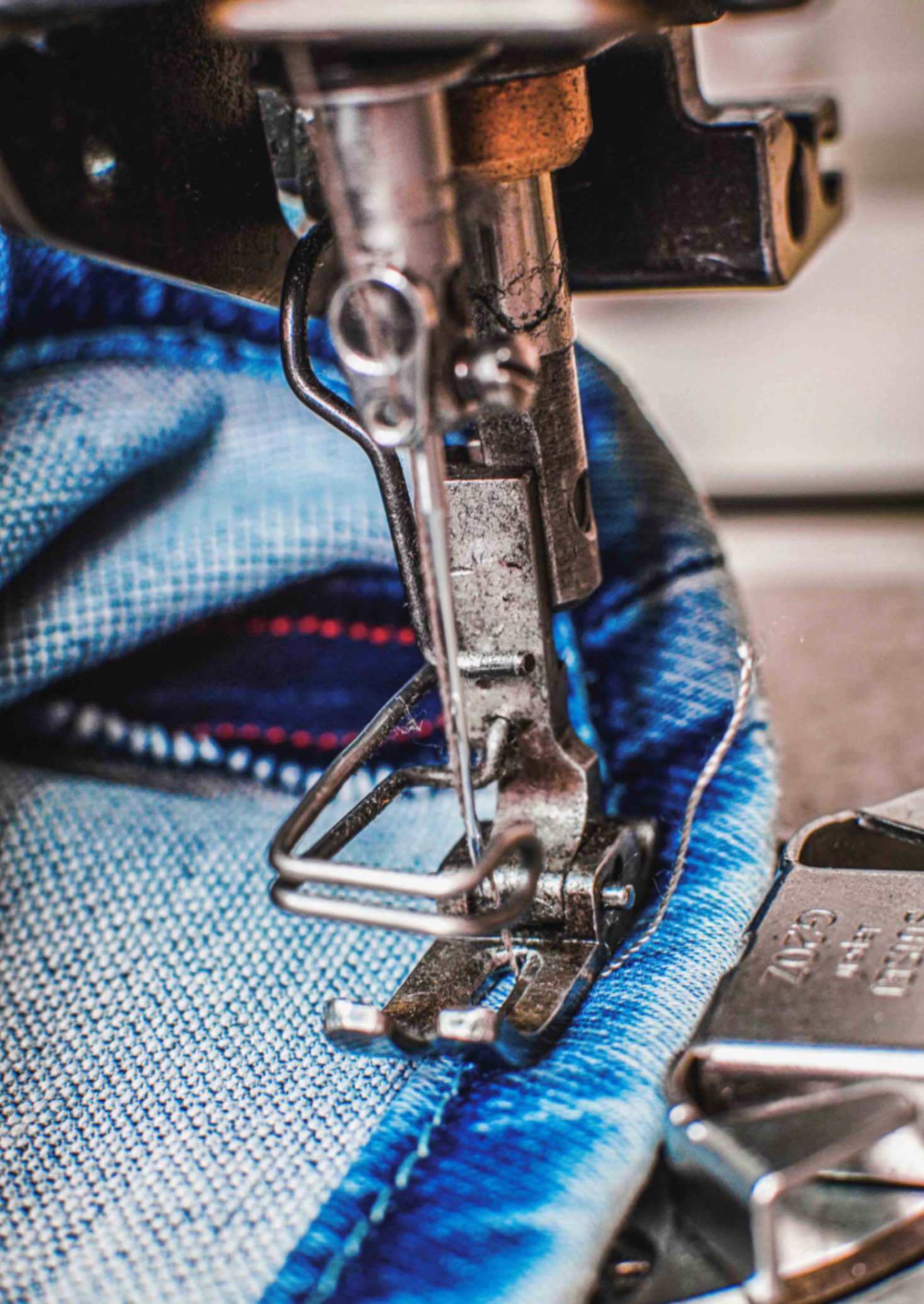 Close-up of a sewing machine stitching a denim hem, highlighting precise craftsmanship and detailed jean production.