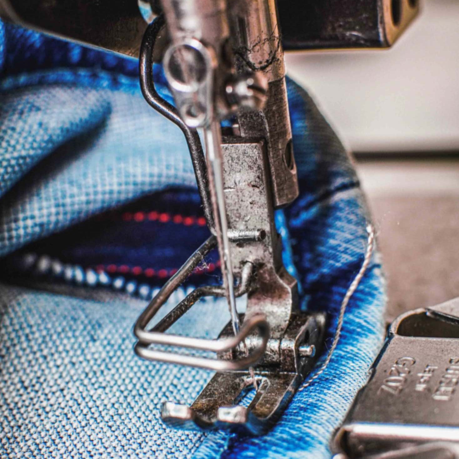 Close-up of a sewing machine stitching a denim hem, highlighting precise craftsmanship and detailed jean production.