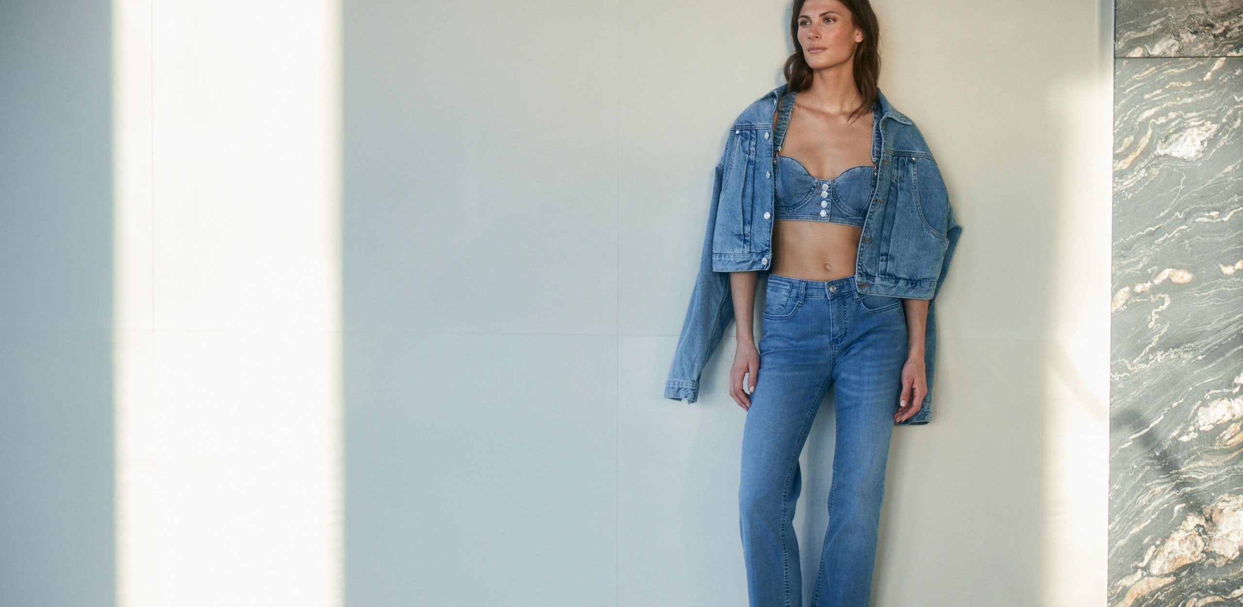 Woman wearing a blue flared denim jeans with matching denim bralette and jacket.