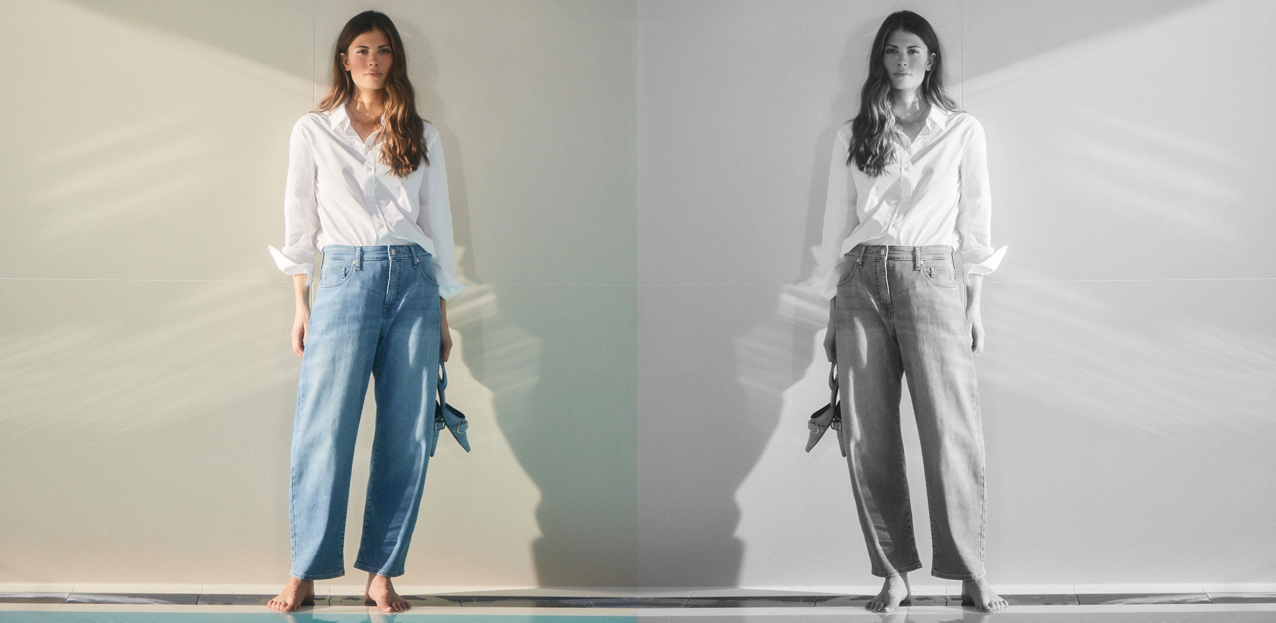 A woman stands barefoot in a white shirt and light blue wide-leg jeans against a sunlit wall, looking at the camera.