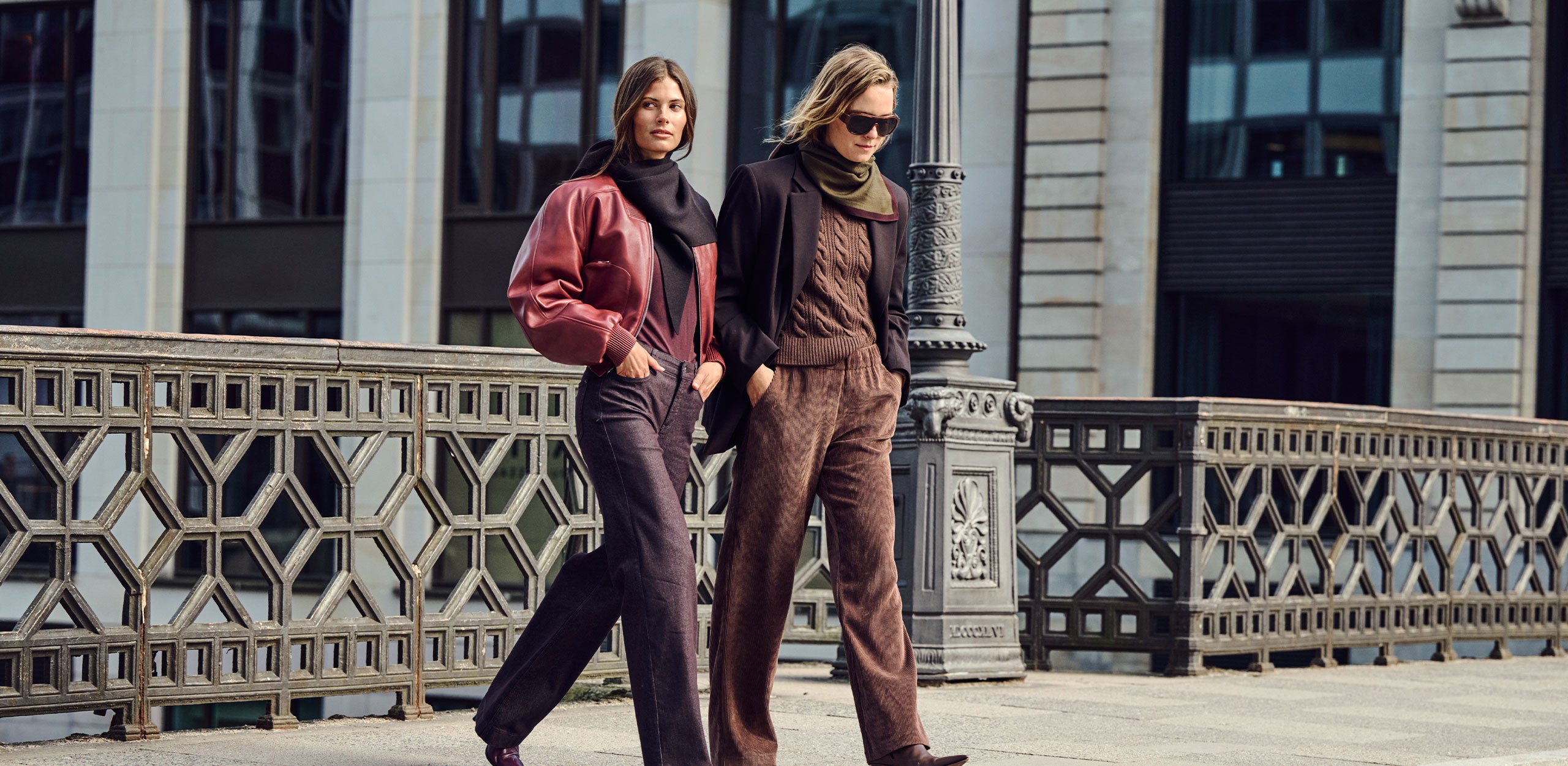 Two women wearing stylish autumn outfits in warm brown and burgundy tones, walking through the city.