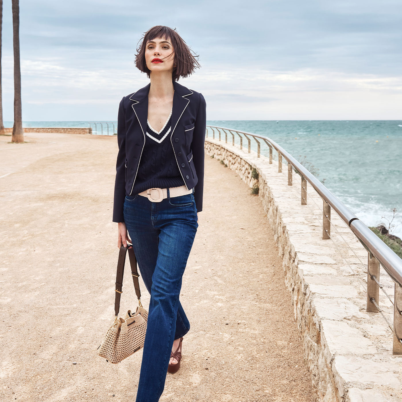 Woman walking along the coast in dark denim and a cropped blazer