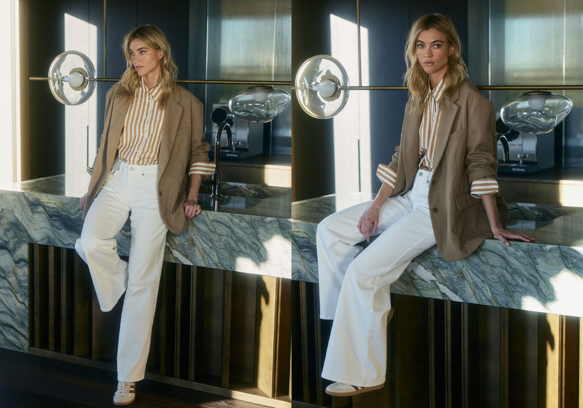 A woman in a striped blouse, beige blazer, and white pants poses by a marble counter in a modern interior.