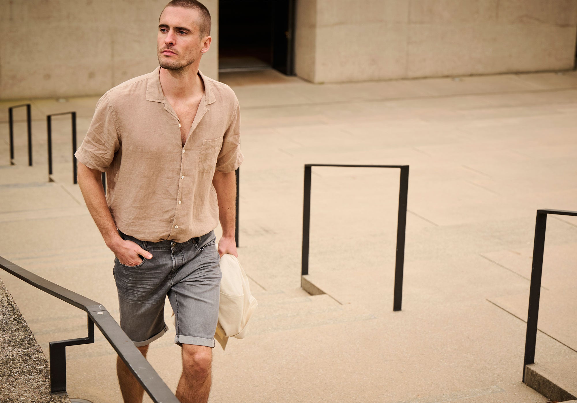 Man wearing a beige linen shirt and grey denim shorts for a relaxed summer look.